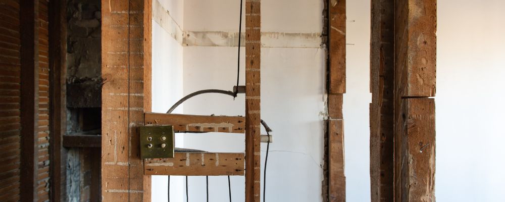 Exposed wall framing with partial wiring in a room under renovation with lath and plaster visible.
