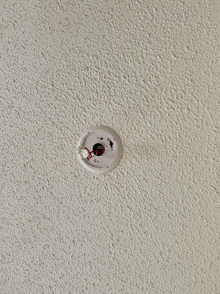 Tankless water heater and electrical conduits mounted on a brick exterior wall with exposed wiring.