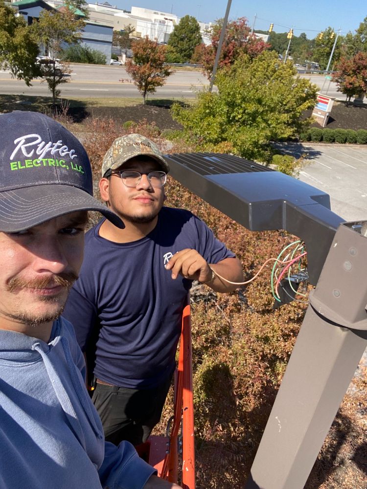 Tankless water heater and electrical conduits mounted on a brick exterior wall with exposed wiring.