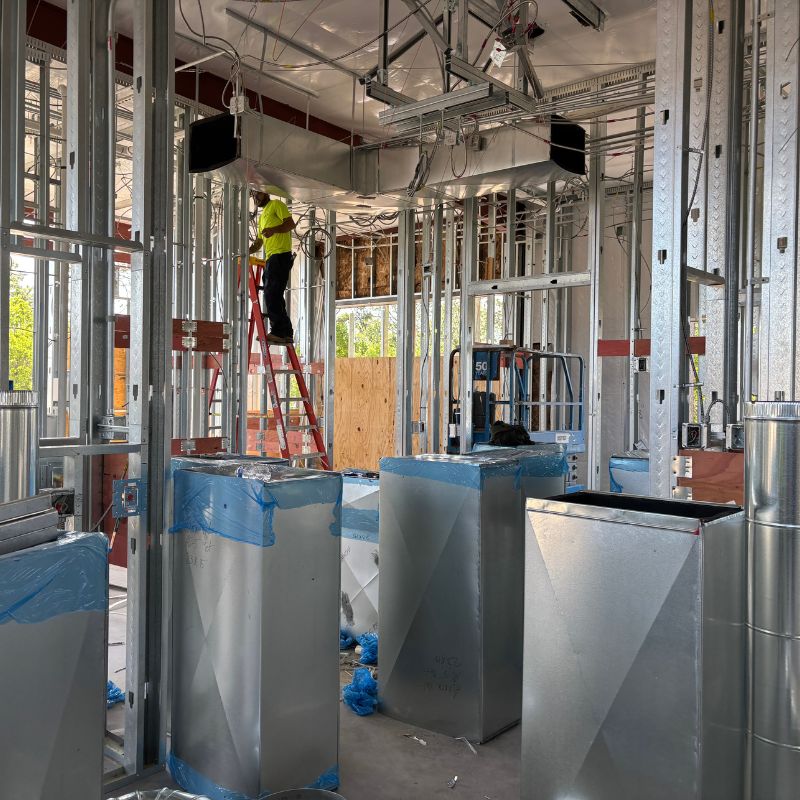 Electrician using a power drill to install wiring in an outdoor electrical panel on a brick wall.