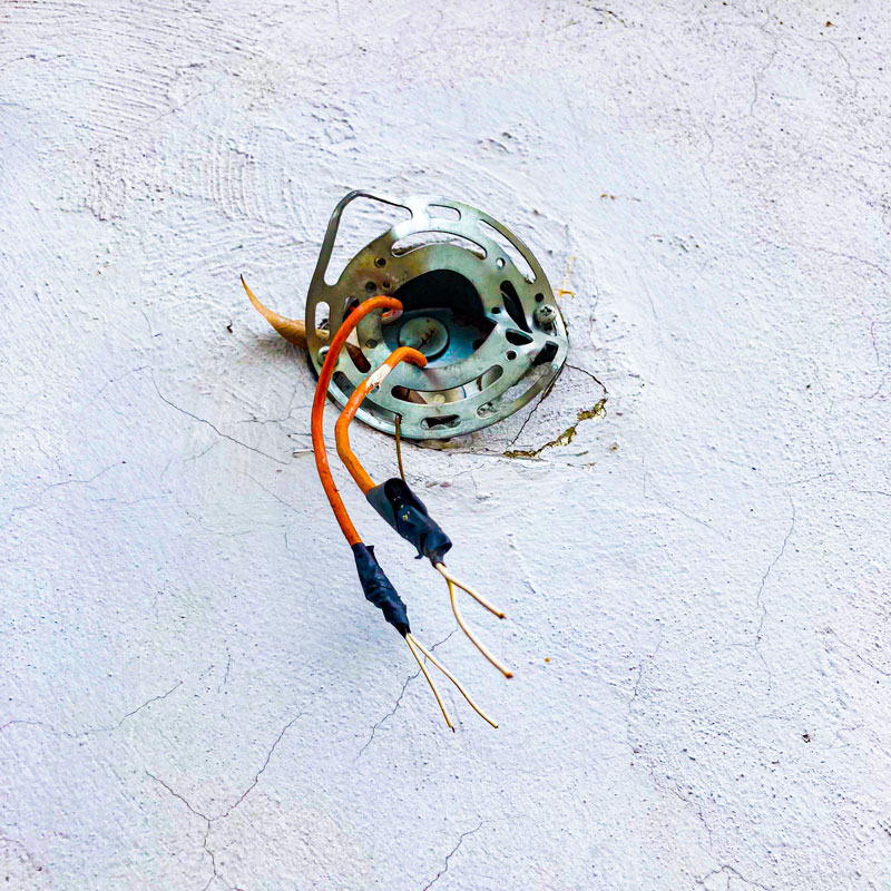 Electrician using a power drill to install wiring in an outdoor electrical panel on a brick wall.